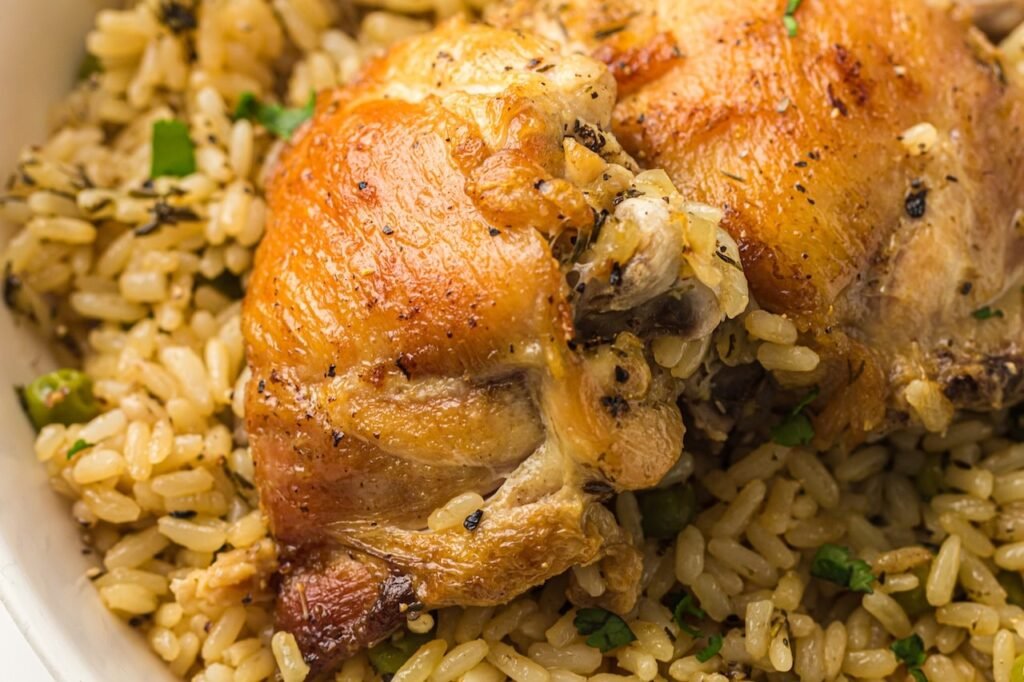 Close-up of golden-brown chicken thighs served over fluffy Instant Pot chicken and rice with green peas and herbs, showing the texture of the cooked rice and crispy chicken skin.