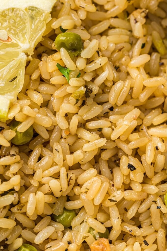 Close-up of fluffy cooked rice from an Instant Pot chicken and rice recipe with green peas, herbs, and a lemon wedge showing the texture of the perfectly cooked rice.