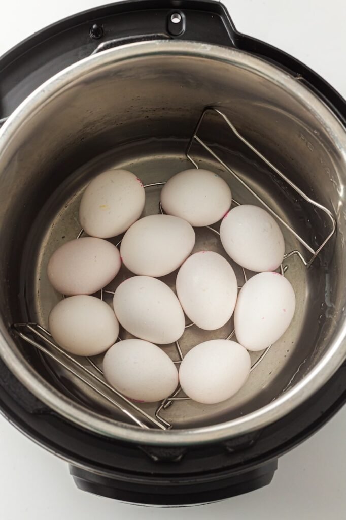 Eggs arranged on a metal trivet inside an Instant Pot with water at the bottom, ready to be pressure cooked.