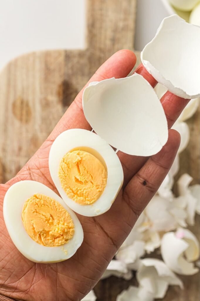 Hand holding peeledeggs with smooth whites and fully cooked yellow yolks, with eggshells removed cleanly.