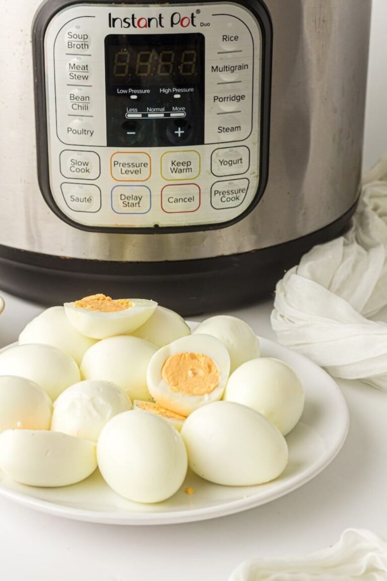 Plate of peeled hard-boiled eggs with bright yellow yolks in front of an Instant Pot, showing the finished results.