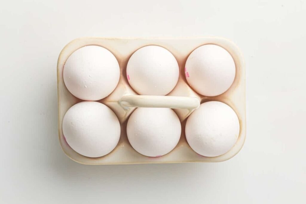 Six raw eggs arranged on a trivet inside an Instant Pot insert, ready to be pressure cooked using the 5-5-5 method.