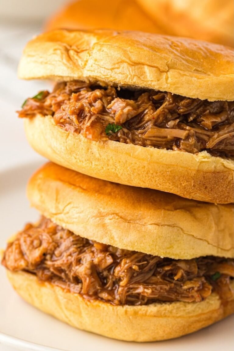Two pulled pork sandwiches stacked on soft sandwich buns, filled with tender shredded BBQ pork made from Instant Pot pulled pork.