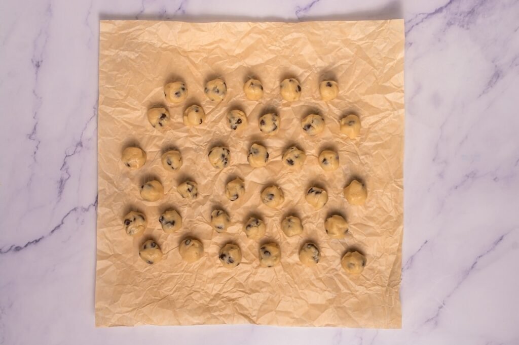 Small balls of edible dough with mini chocolate chips arranged on parchment paper for topping.