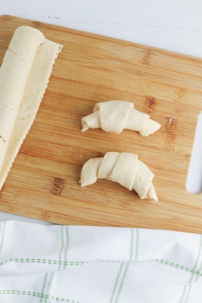 Dough triangles rolled into crescent shapes on a wooden cutting board while preparing.