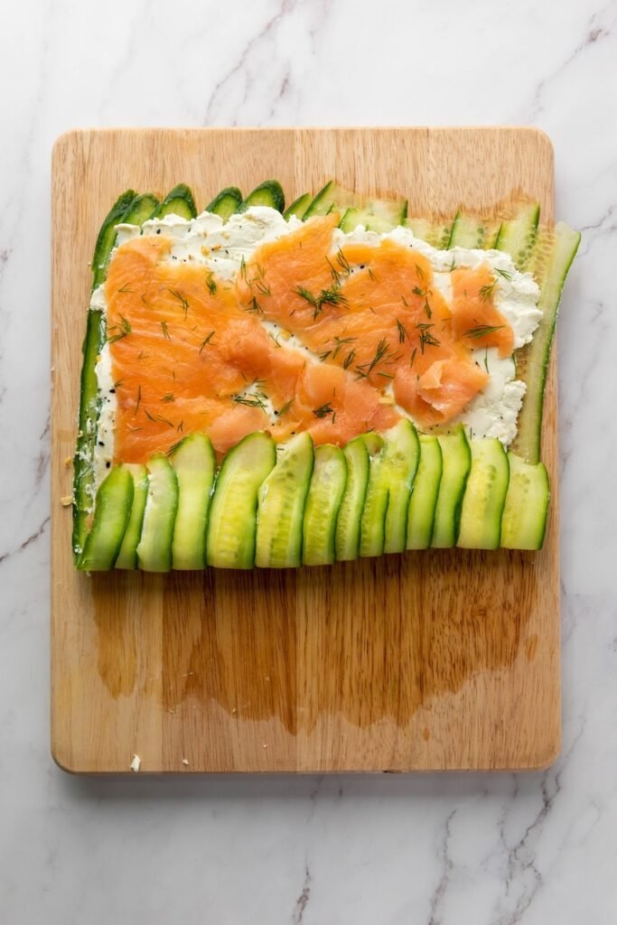 ribbons layered with cream cheese, smoked fish, and dill being rolled on a cutting board.