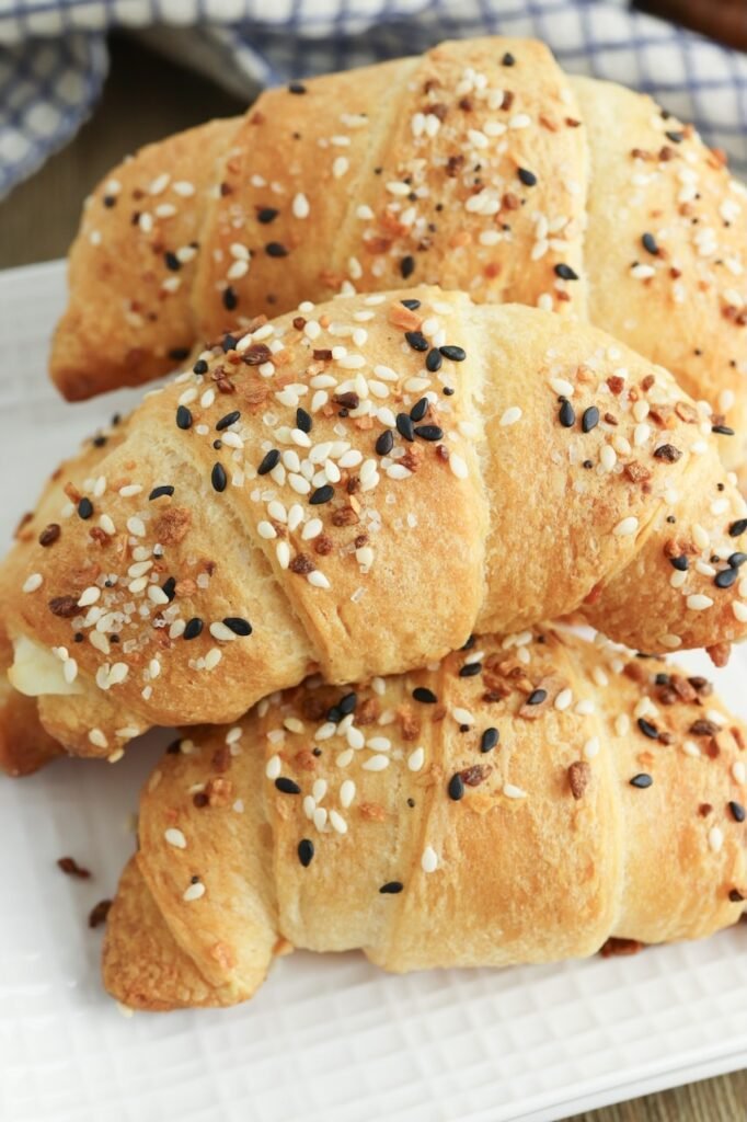 Close-up of flaky everything bagel crescent rolls baked until golden brown and topped with sesame seeds, poppy seeds, garlic, and onion seasoning on a white serving plate.