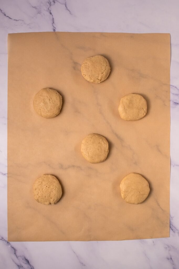 Overhead view of six scoops of cookie dough spaced apart on parchment paper on a marble countertop, prepared for baking.