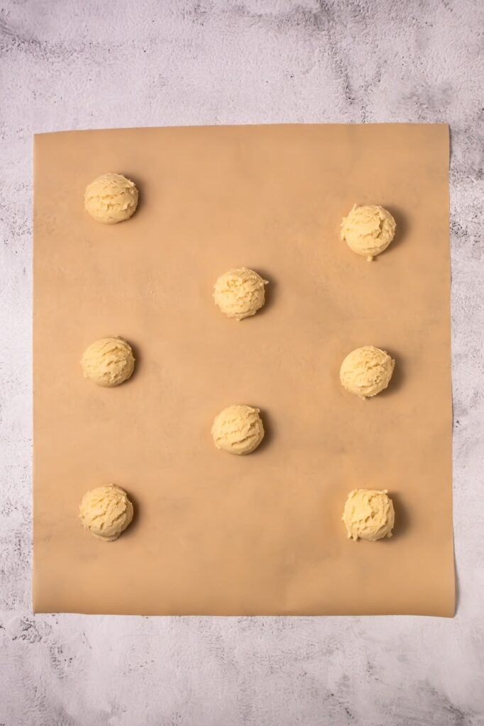 Scoops of coconut lime cookie dough spaced on parchment paper before baking thick bakery-style cookies.