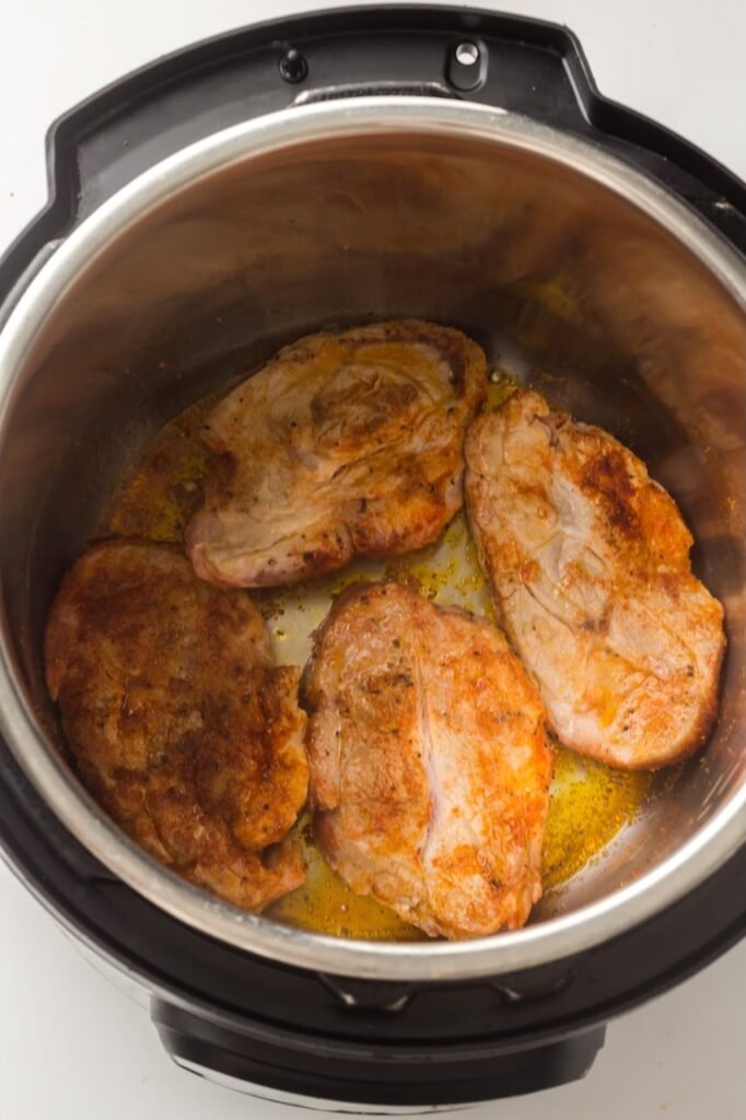 Seasoned shoulder steaks browning in olive oil inside an during the sauté step.