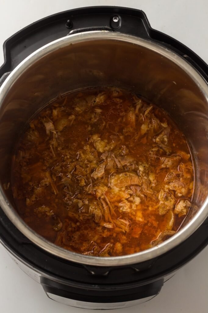 Shredded pork shoulder sitting in rich cooking juices inside an Instant Pot after pressure cooking for Instant Pot pulled pork.