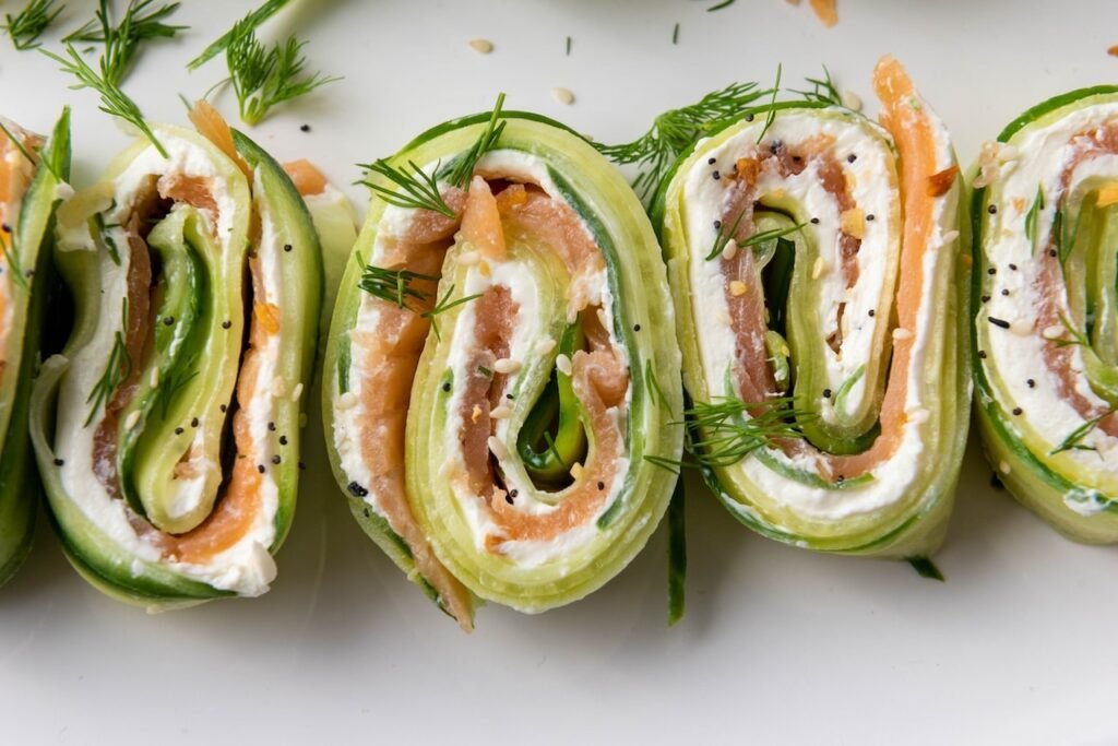 Extreme close-up of smoked salmon cucumber rolls showing spiral layers of cucumber ribbons, cream cheese filling, smoked salmon, fresh dill, and everything bagel seasoning.