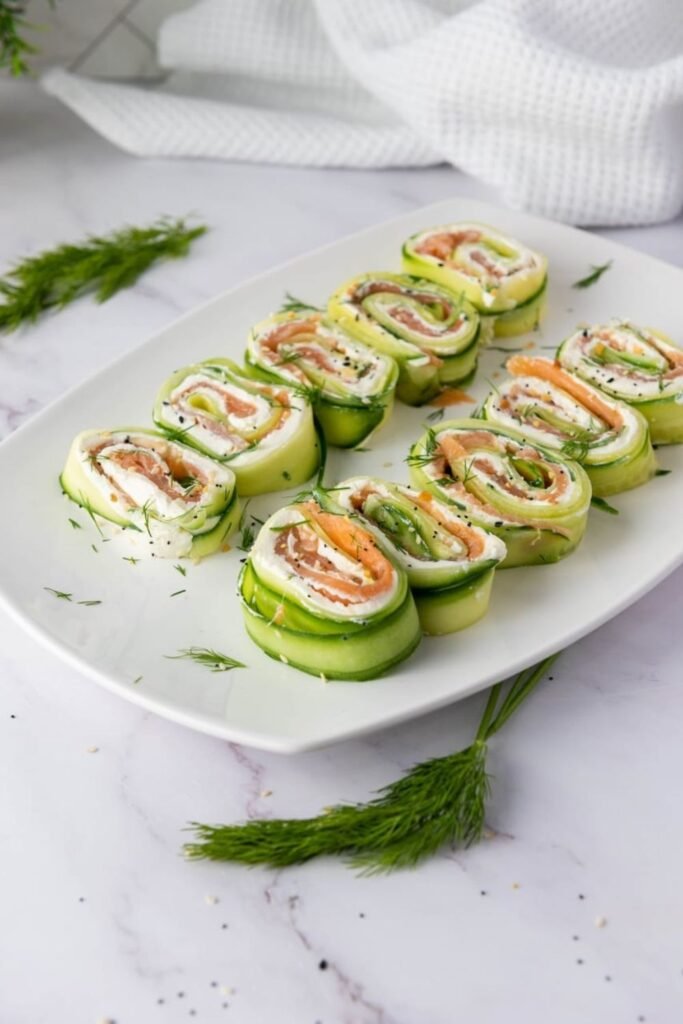 Plated smoked salmon cucumber rolls made with thin cucumber ribbons, cream cheese, smoked salmon, and fresh dill, sliced into bite-size appetizer pinwheels.
