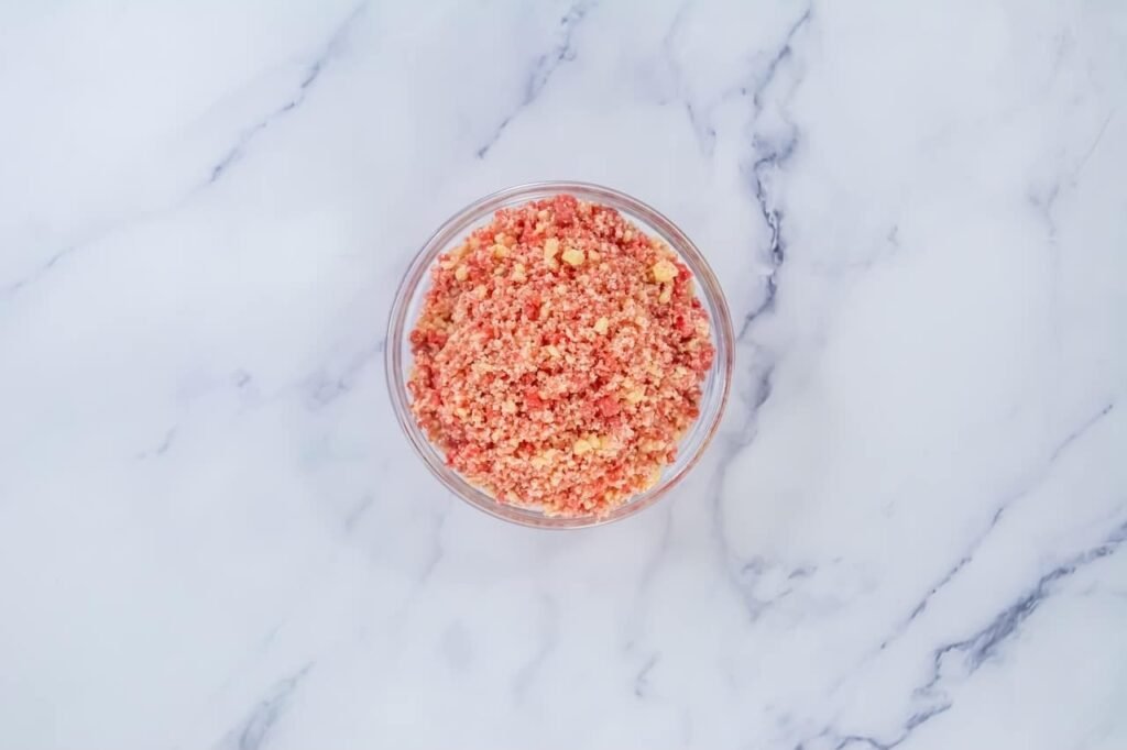 Small bowl filled with strawberry and vanilla crumble topping mixed together, showing a crumbly texture ready to use on strawberry shortcake cookies.