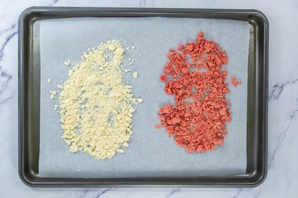 Baked strawberry and vanilla streusel crumbles on a parchment-lined baking sheet, showing lightly toasted texture for strawberry shortcake cookies.