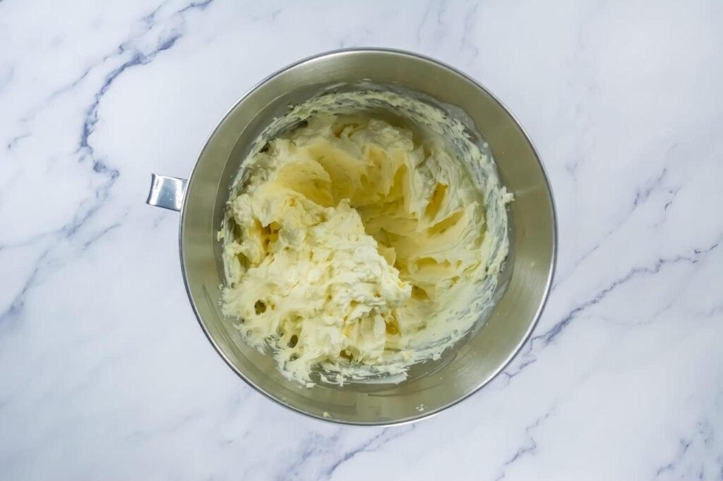 Mixing bowl with whipped cream cheese frosting, showing a smooth and fluffy texture ready for topping strawberry shortcake cookies.