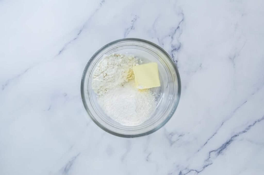 Glass bowl with butter, flour, and vanilla pudding mix used to make a crumbly streusel topping.