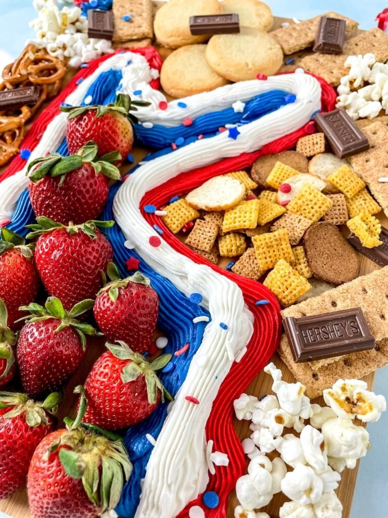 Close-up angle of a 4th of July buttercream board with red, white, and blue frosting, strawberries, cookies, graham crackers, chocolate pieces, pretzels, and popcorn.
