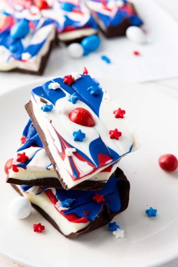 Close-up of stacked red, white, and blue chocolate bark pieces with sprinkles and candy on a white plate, showing the finished patriotic dessert.