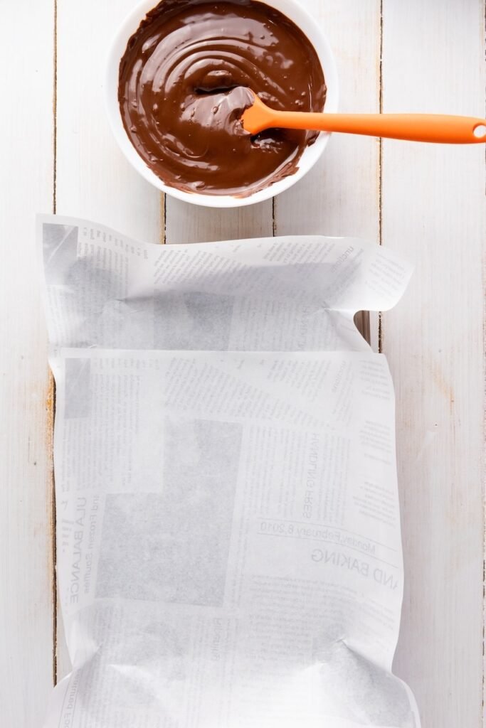Overhead view of a parchment-lined baking pan next to a bowl of melted chocolate, showing the preparation step before spreading the chocolate for 4th of July chocolate bark.