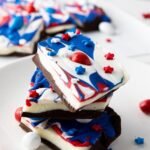 Stacked pieces of red, white, and blue chocolate bark topped with sprinkles and candy on a white plate, showing the finished 4th of July dessert.