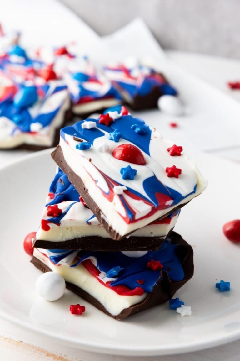 Stacked pieces of red, white, and blue chocolate bark topped with sprinkles and candy on a white plate, showing the finished 4th of July dessert.