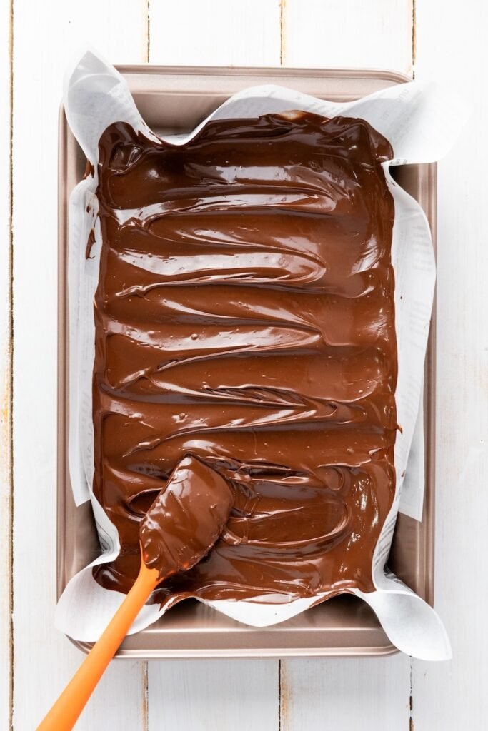 Melted semi-sweet chocolate spread into an even layer on a parchment-lined baking sheet, showing the first layer of chocolate for 4th of July chocolate bark.