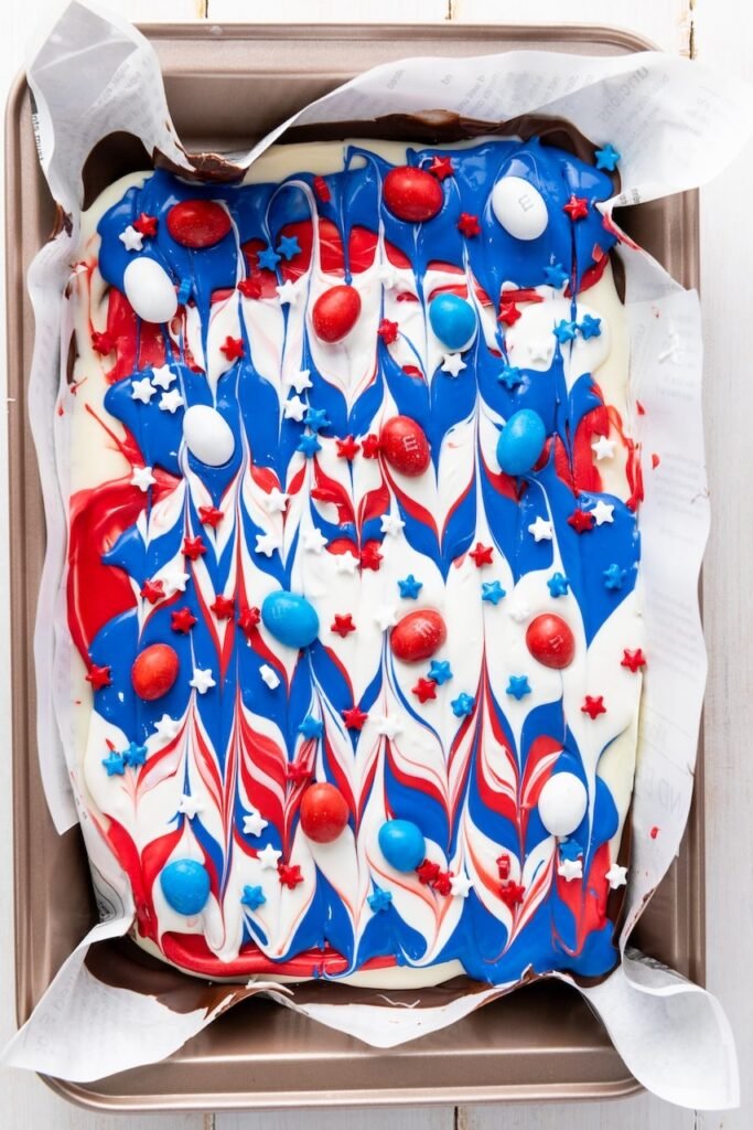 Finished dessert with red, white, and blue swirls topped with star sprinkles and candy-coated chocolates on a parchment-lined baking sheet.