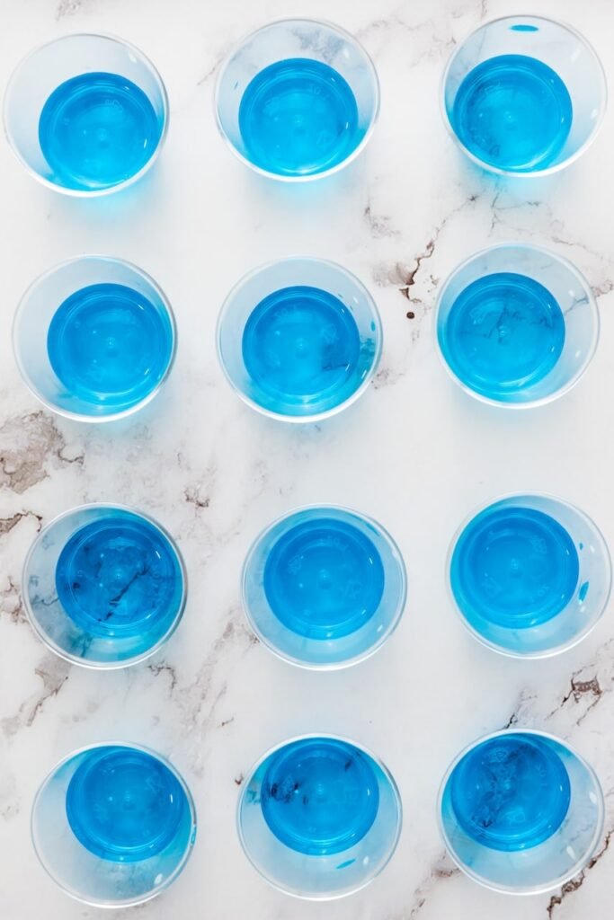 Overhead view of small plastic cups filled with bright blue 4th of July jello shots arranged in neat rows on a marble countertop