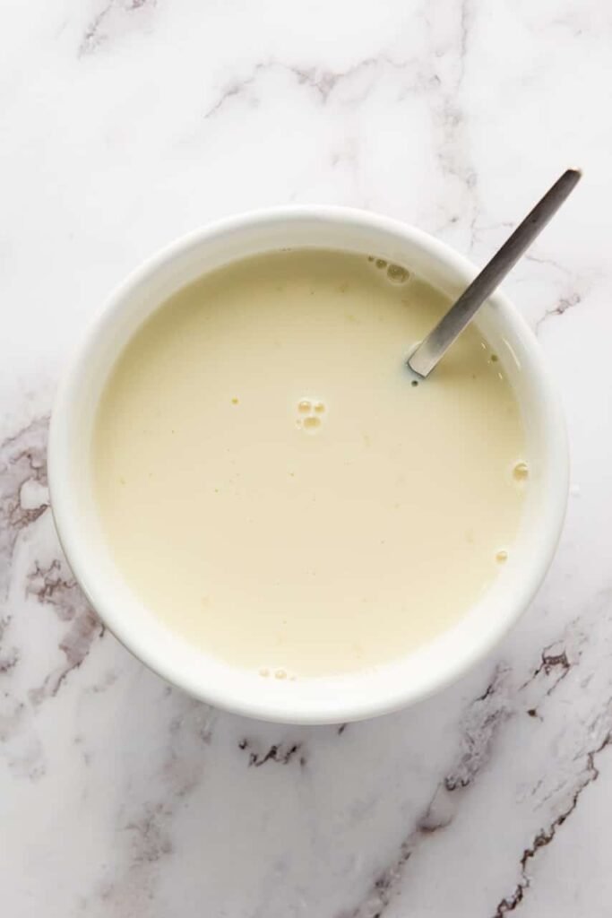 Overhead view of a smooth creamy mixture being stirred in a bowl for the white layer on a marble countertop