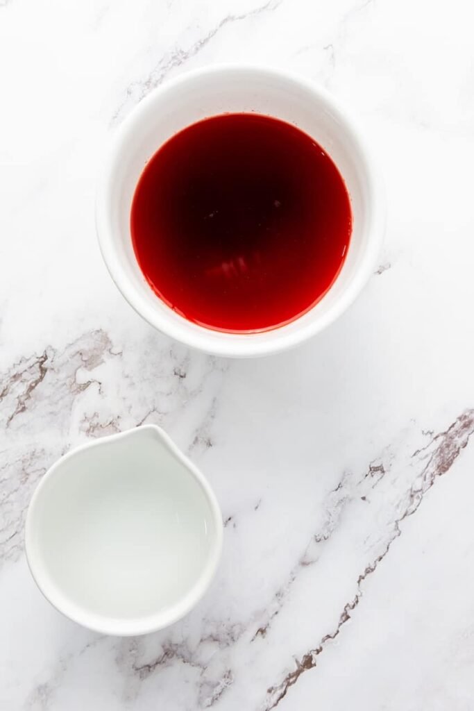 Partially visible bowl of red gelatin mixture with distorted background, intended to show the red layer preparation.