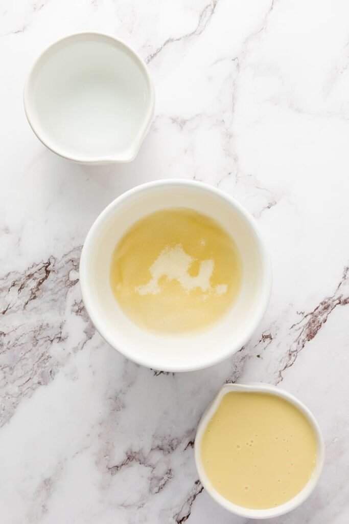Close-up of vodka bottle next to a bowl of sweetened condensed milk used for making 4th of July jello shots on a marble surface