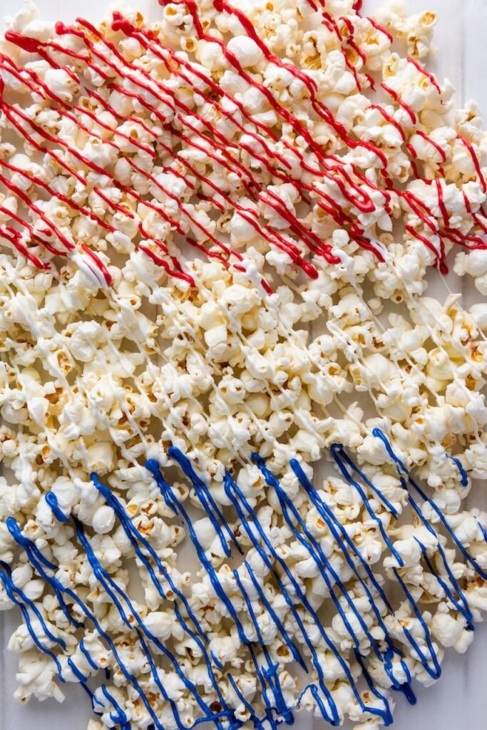 Close-up of popcorn covered with red, white, and blue candy drizzle, showing a festive 4th of July popcorn snack spread out on parchment paper.