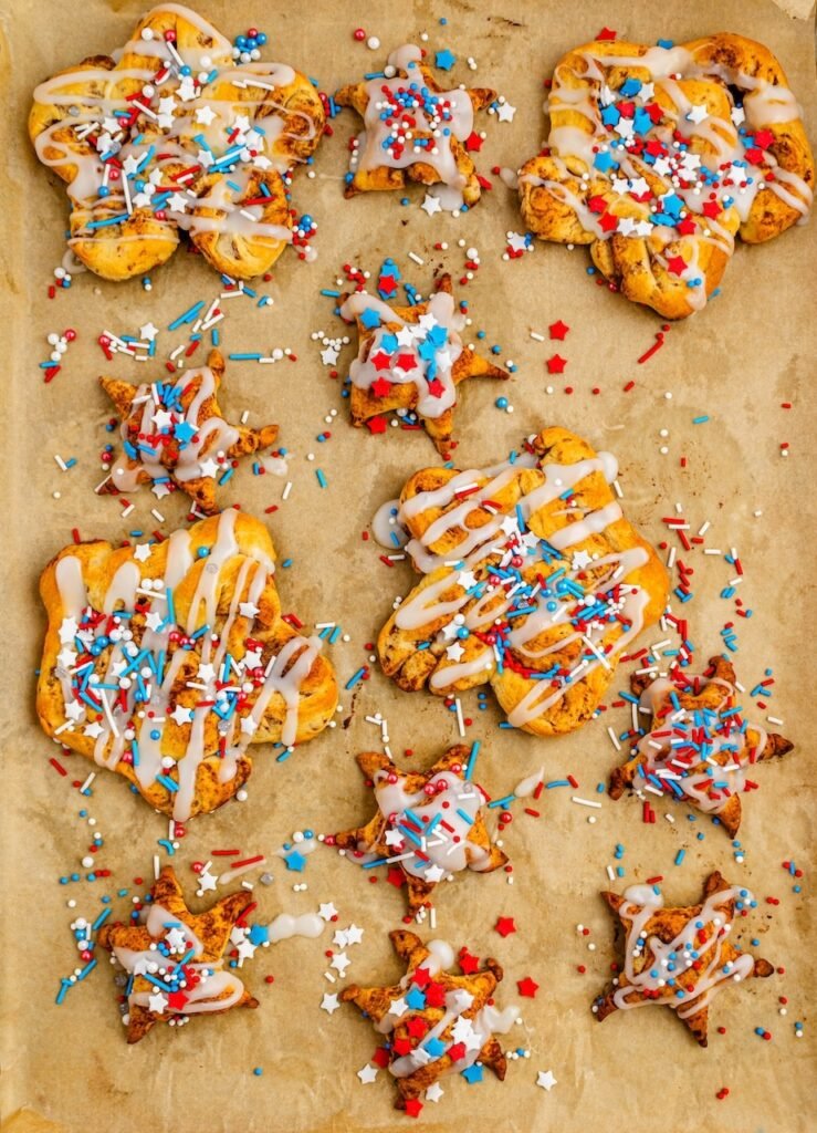 Overhead view of baked dessert drizzled with icing and topped with red, white, and blue sprinkles on a parchment-lined baking sheet.