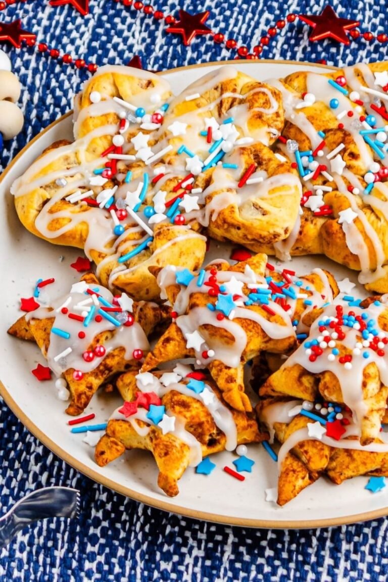 Plate of star-shaped cinnamon rolls drizzled with icing and topped with red, white, and blue sprinkles, set on a festive patriotic background.