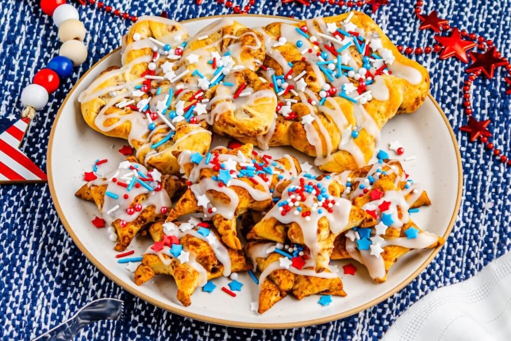Plate filled with star-shaped cinnamon rolls drizzled with icing and topped with red, white, and blue sprinkles on a patriotic table setting.