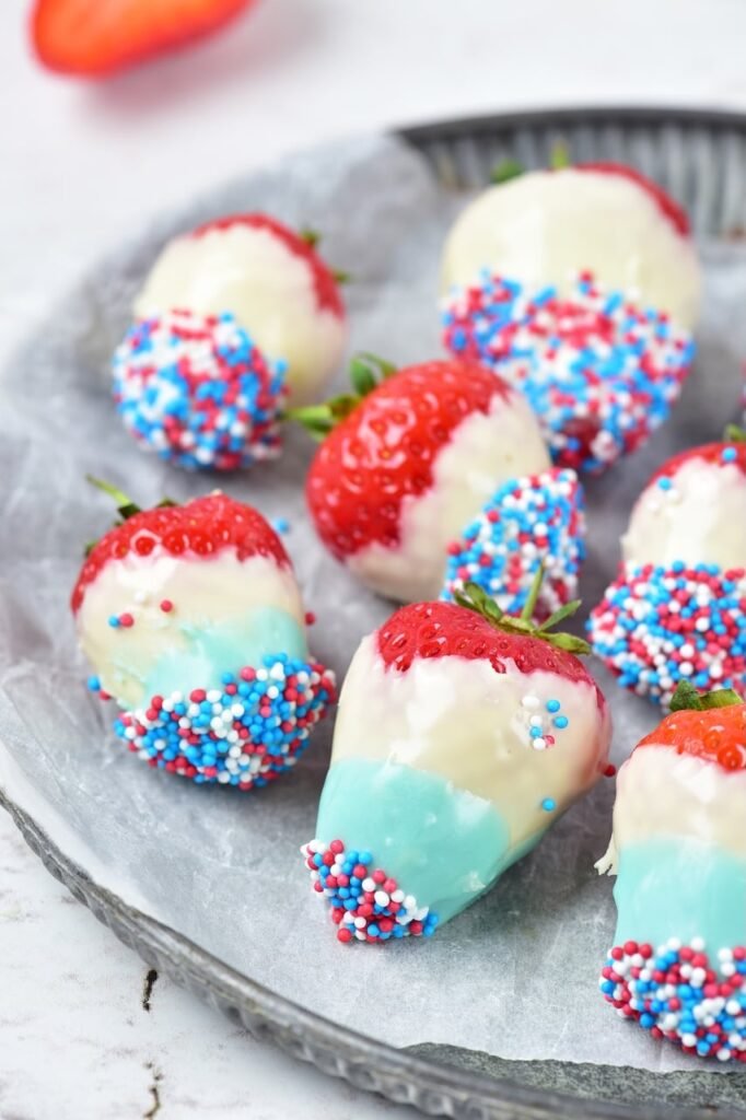 Close-up view of 4th of july strawberries dipped in white and blue chocolate and coated with red, white, and blue sprinkles on a serving plate.