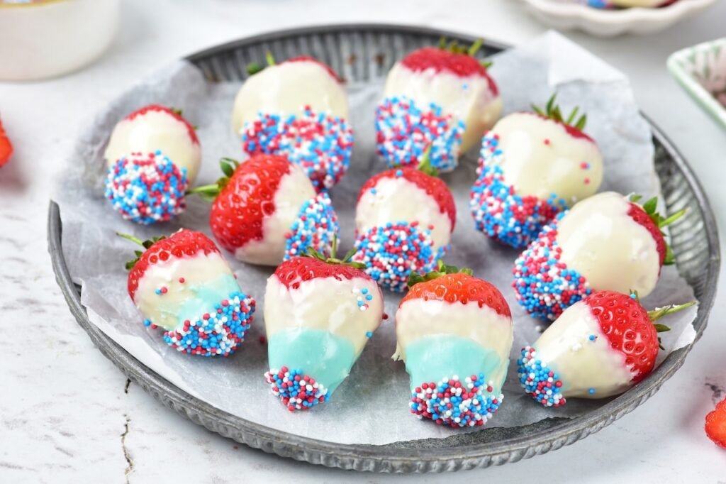 Close-up view of 4th of july strawberries dipped in white and blue chocolate and coated with red, white, and blue sprinkles on a serving plate.