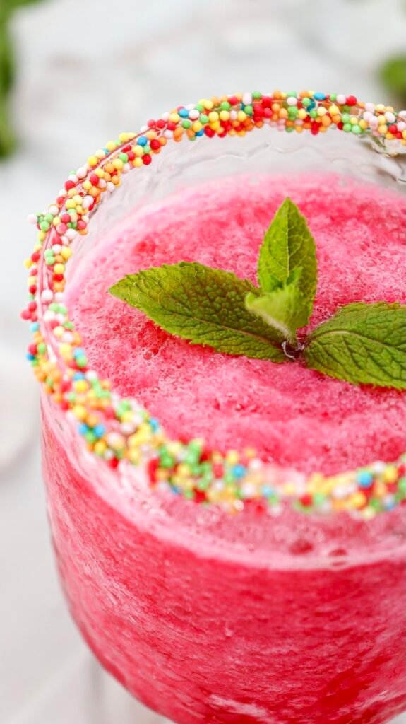 Close-up of a watermelon slushie with a smooth icy texture, topped with fresh mint and a colorful sprinkle rim