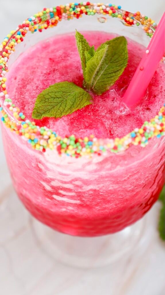 Close-up of a watermelon slushie with a pink straw, fresh mint garnish, and colorful sprinkle rim in a glass