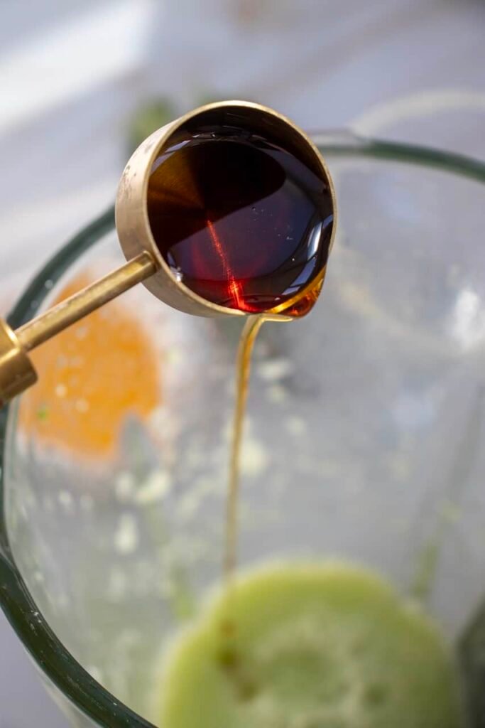 Close-up of agave syrup being poured into a blender with cucumber puree while making a cucumber margarita mocktail, showing a key step in mixing the drink.