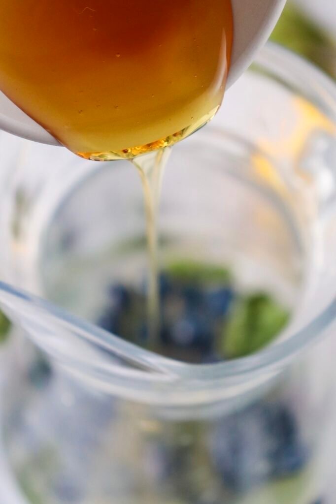 Honey being poured into a glass with blueberries and mint to sweeten mixture.