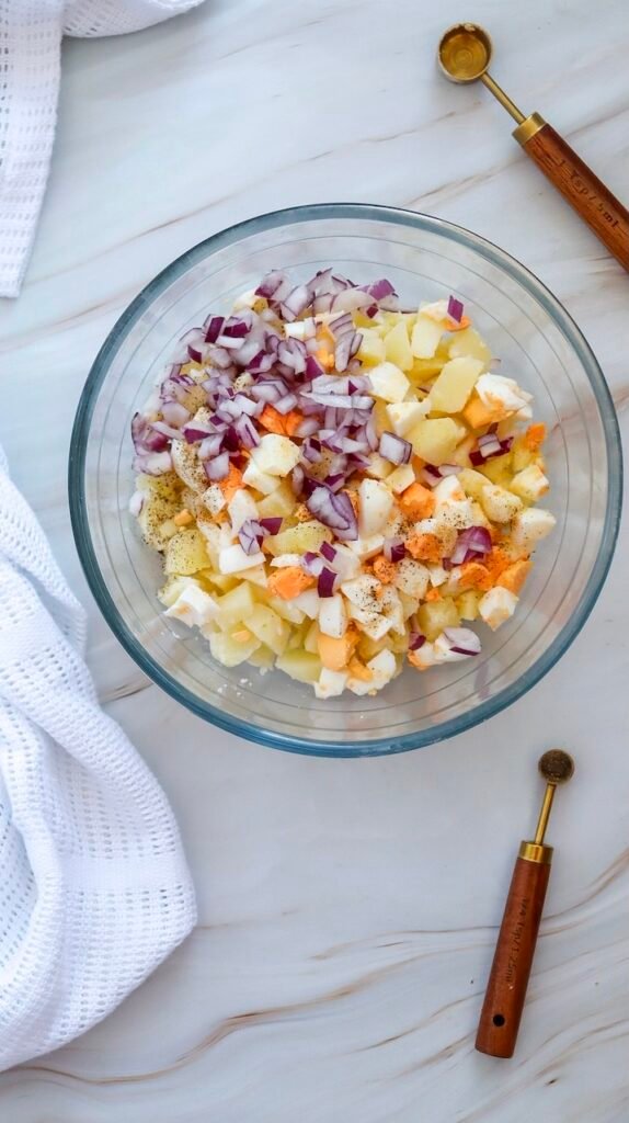 Chopped red onion added to a bowl of potatoes and hard-boiled eggs, preparing ingredients for side dish