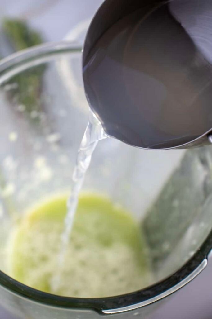 Close-up of sparkling water being poured into a blender with cucumber mixture to finish a beverage, showing the step that adds fizz.