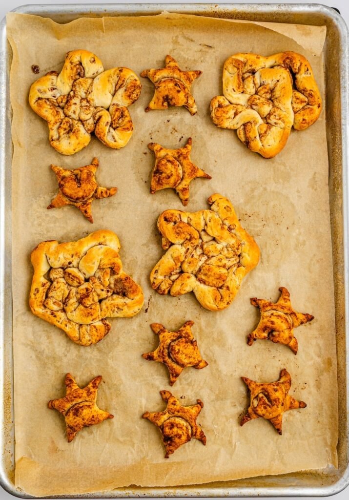 Overhead view of baked breakfast on a parchment-lined baking sheet, golden brown with visible cinnamon swirls and slightly puffed edges.