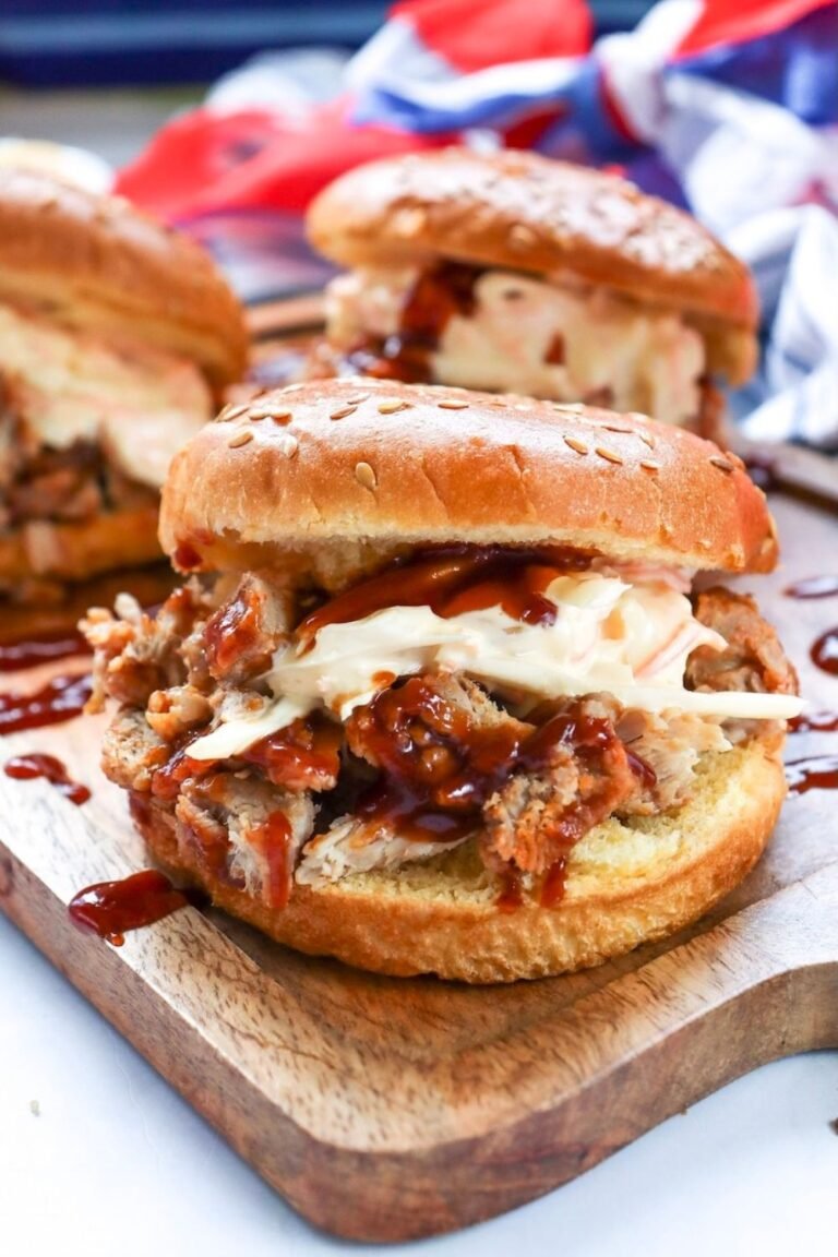 Close-up of a BBQ pulled pork sandwich with shredded pork, barbecue sauce, and creamy coleslaw on a sesame seed bun, served on a wooden board.