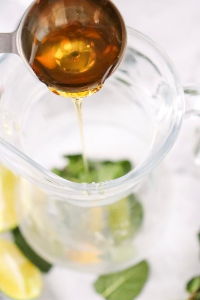 Agave syrup being poured into a glass with mint and lime while making a blackberry mojito mocktail