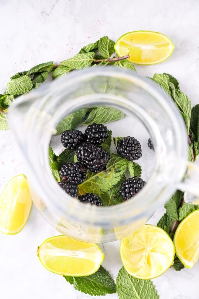 Fresh blackberries and mint leaves inside a glass before muddling, surrounded by lime wedges for a blackberry mojito mocktail