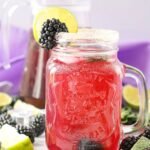 Mason jar filled with a blackberry mojito mocktail with ice, mint, and a blackberry and lime garnish on the rim