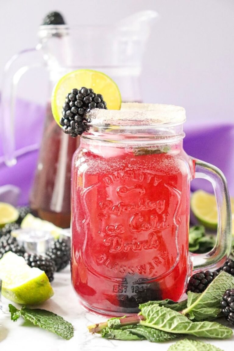 Mason jar filled with a blackberry mojito mocktail with ice, mint, and a blackberry and lime garnish on the rim